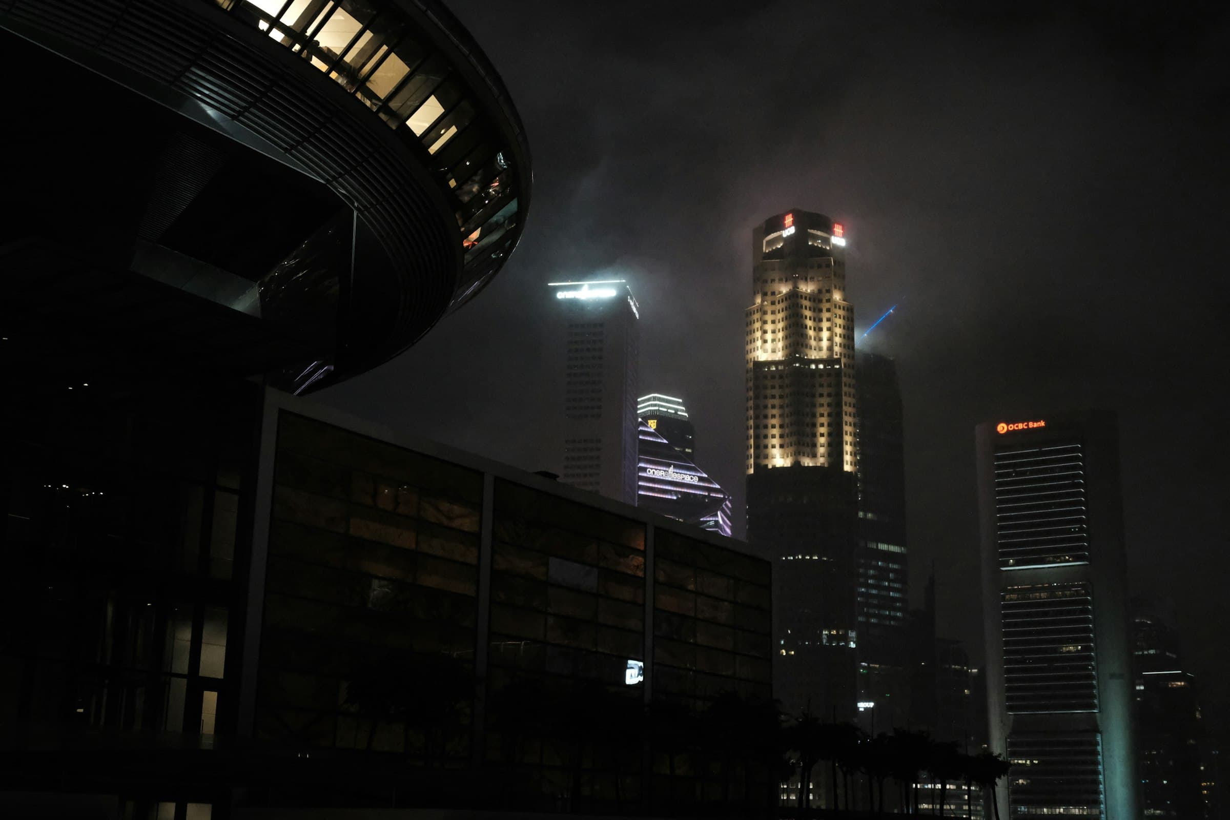 Singapore's financial district at night, towers disappearing into low cloud